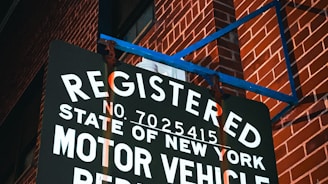 A sign reads 'Registered Motor Vehicle Repair Shop, State of New York' and is mounted against a red brick wall. The scene is illuminated by ambient lighting, casting shadows on the text and the wall.